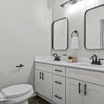 Contemporary bathroom with white cabinets and black fixtures, modern mirror, and minimalist design.