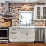 Brushed white kitchen cabinets with stainless steel appliances and a brick backsplash.