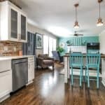 Bright modern kitchen with white cabinetry and teal accents, open-concept living area with hardwood flooring.