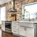 Modern white kitchen cabinets with farmhouse sink and brick wall backdrop in premium cabinet design.