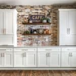 Modern white kitchen cabinets with built-in storage and minimalist handles, set against an exposed brick wall.