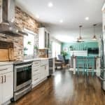 Modern kitchen with white custom cabinets, exposed brick walls, and stainless steel appliances.