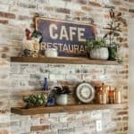 Rustic wood shelves with decorative items against exposed brick wall in a cafe or restaurant setting.