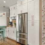 Sleek white kitchen cabinets with gold handles and stainless steel refrigerator in modern kitchen.