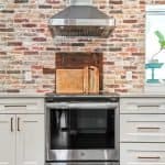 Sleek stainless steel kitchen stove with modern cabinets and brick wall backdrop.