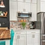 Sleek white kitchen cabinets with modern design and brushed bronze hardware, featuring a brick backsplash and stainless steel appliances.