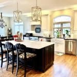 Elegant kitchen cabinetry with a mix of white and dark wood cabinets, stylish lighting, and modern appliances in a spacious, bright design.