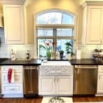 Elegant white kitchen cabinets with dark countertops and a farmhouse sink, featuring custom woodwork and decorative molding.