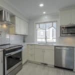 Modern white kitchen cabinets with stainless steel appliances and decorative backsplash.