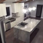 Contemporary white kitchen with marble island, modern pendant lighting, and sleek cabinetry.