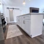 Modern white kitchen island with gold hardware, farmhouse style cabinets, and wooden flooring.