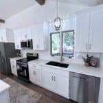 Bright white kitchen cabinets, modern black sink, and stainless steel appliances in a luxury kitchen remodel.