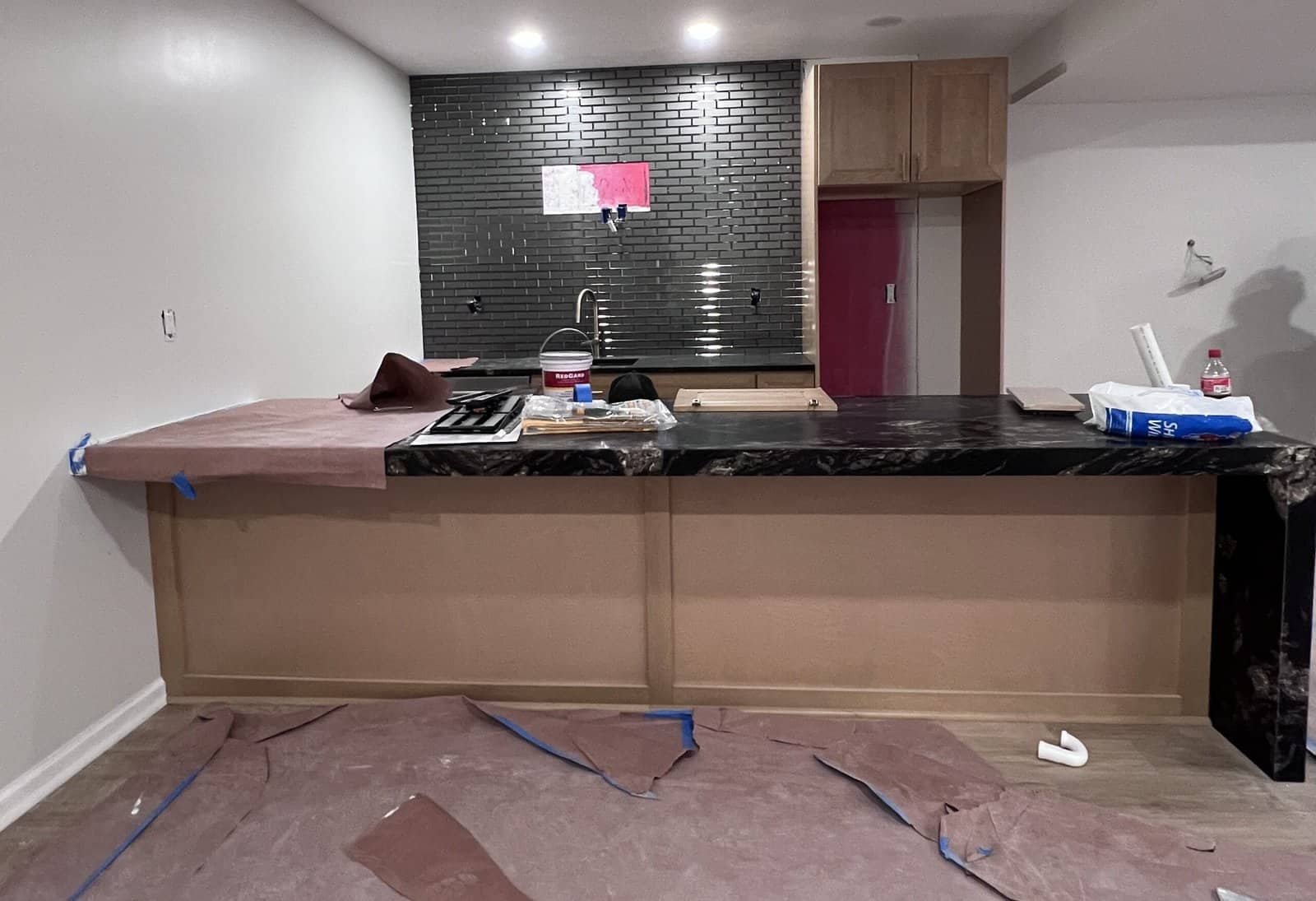 Black marble waterfall-edge countertop with matching brick subway tile backsplash, in-progress wet bar remodel with natural wood cabinetry in Overland Park, KS