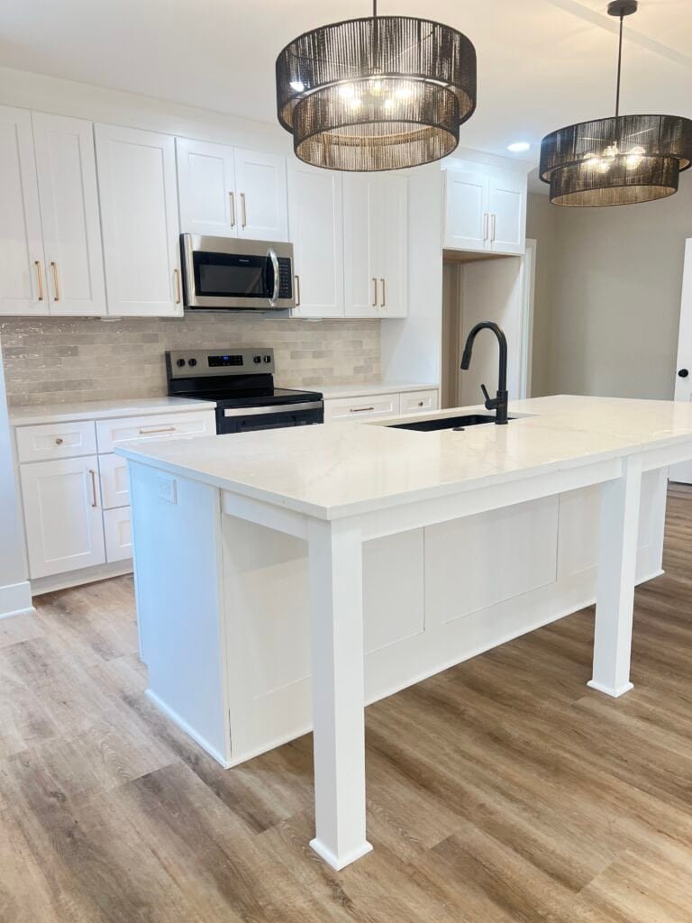 Angled view of white shaker kitchen with quartz island, black pendant lights, and stainless range — Merriam, KS remodel