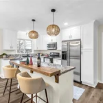 Kitchen island with wood bar top, bar seating, and pendant lighting in a Raytown, MO kitchen remodel with granite counters and stainless refrigerator