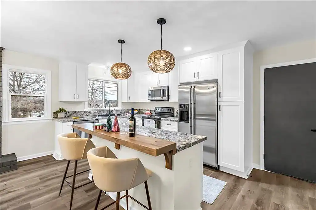 Kitchen island with wood bar top, bar seating, and pendant lighting in a Raytown, MO kitchen remodel with granite counters and stainless refrigerator