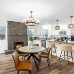 Open concept kitchen remodel in Raytown, MO with white cabinets, granite waterfall island, and view to dining area with brick fireplace