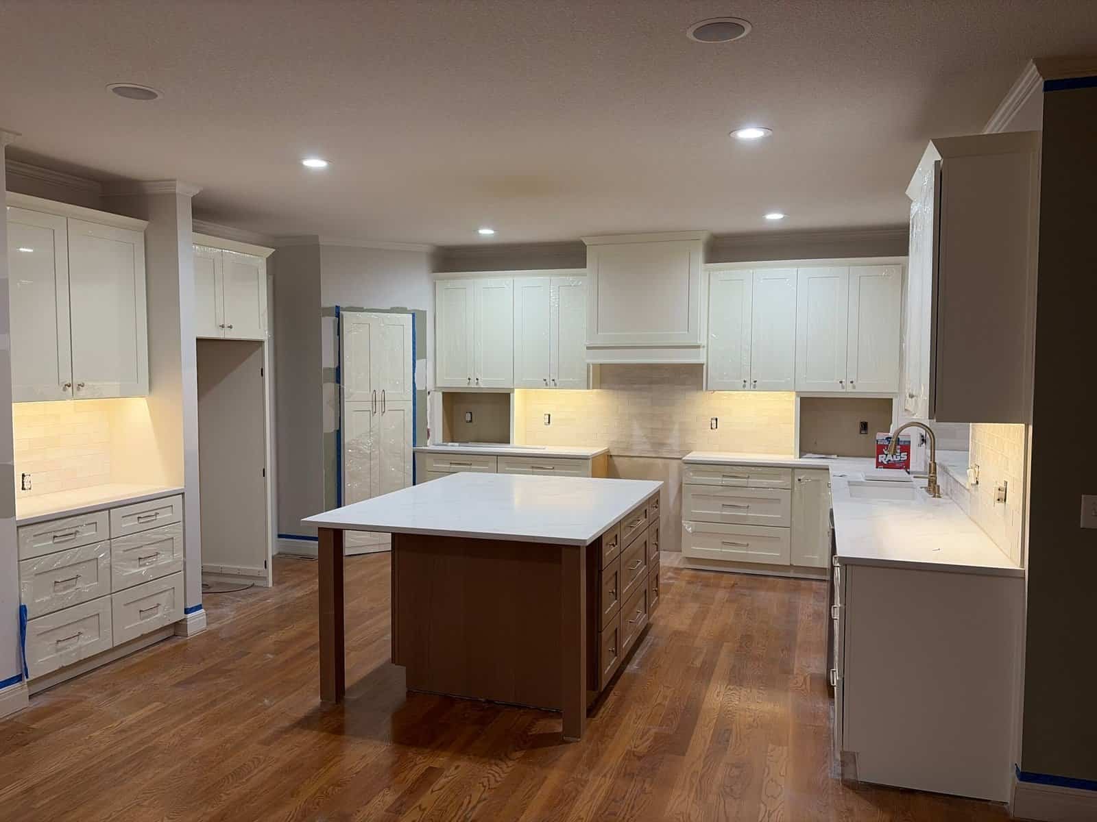 White shaker kitchen with white oak island, quartz countertops, and under-cabinet lighting during a remodel in Shawnee, KS