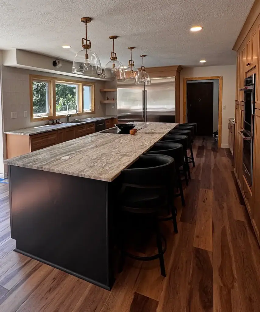 Kitchen remodel Parkville MO with black island, natural stone countertop, built-in appliances, and warm wood cabinets