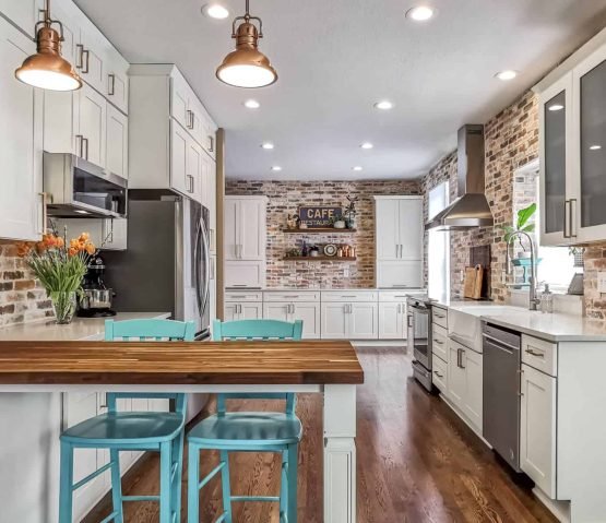 Modern kitchen with white cabinets, brick accents, stainless steel appliances, a wood island, and turquoise chairs in Overland Park, KS.