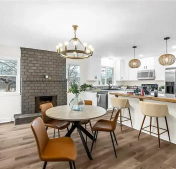 Open concept kitchen remodel in Raytown, MO with white cabinets, granite waterfall island, and view to dining area with brick fireplace